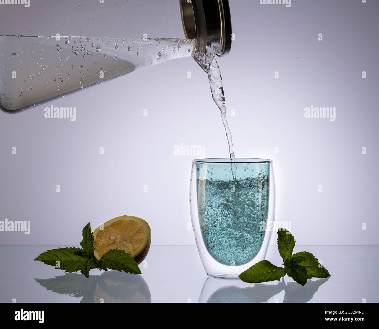 Wasser aus Glasdekanter auf transparentem hellblauem Hintergrund in Glas gießen, sauberes Wasser trinken, Konzept. Stockfoto