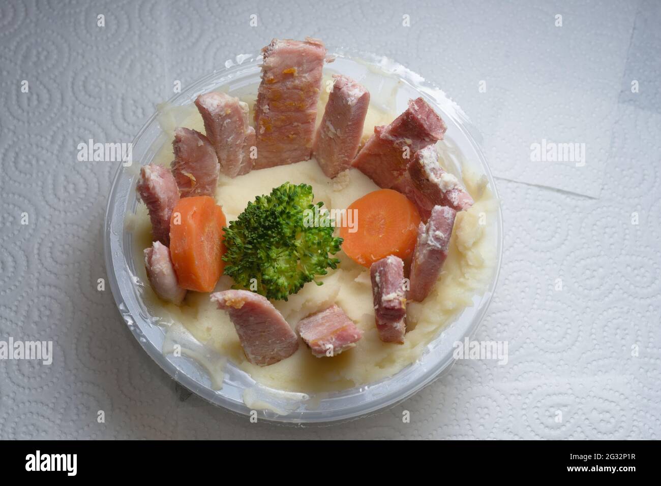 Eine Wanne Kartoffelbrei auf einer weißen Küchenrolle. Ungewöhnliche Präsentation von Fleisch und Gemüse. Hausgemachte Variante einer Supermarktmahlzeit Stockfoto
