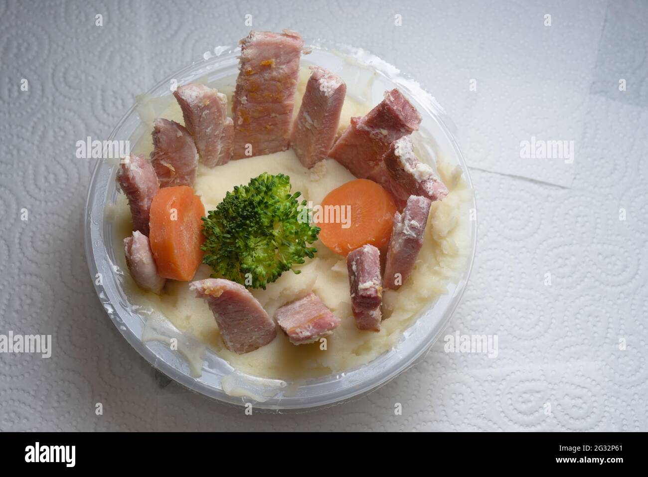 Plastikbehälter mit Kartoffelpüree, Gemüse und Gammon. Gammon in dünne Streifen geschnitten und in einem Kreis angeordnet. Künstlerisches Essen Stockfoto