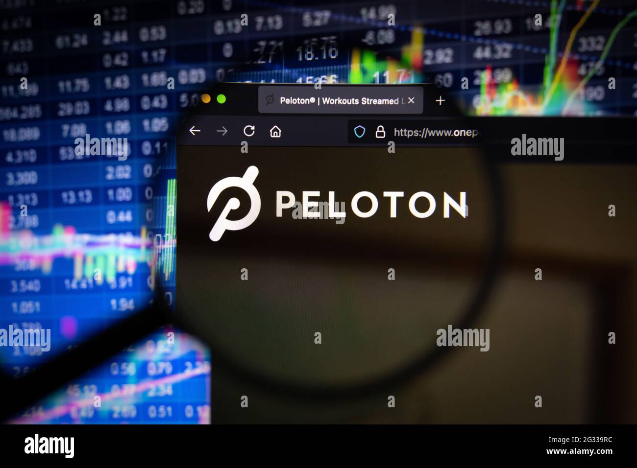 Peleton-Firmenlogo auf einer Website mit verschwommenen Börsenentwicklungen im Hintergrund, auf einem Computerbildschirm durch eine Lupe gesehen Stockfoto