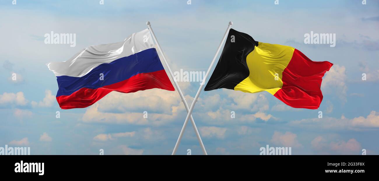 Flaggen von Russland und Belgien winken im Wind auf Fahnenmasten gegen den Himmel mit Wolken am sonnigen Tag. Symbolisieren Beziehung, Dialog zwischen zwei Countris Stockfoto