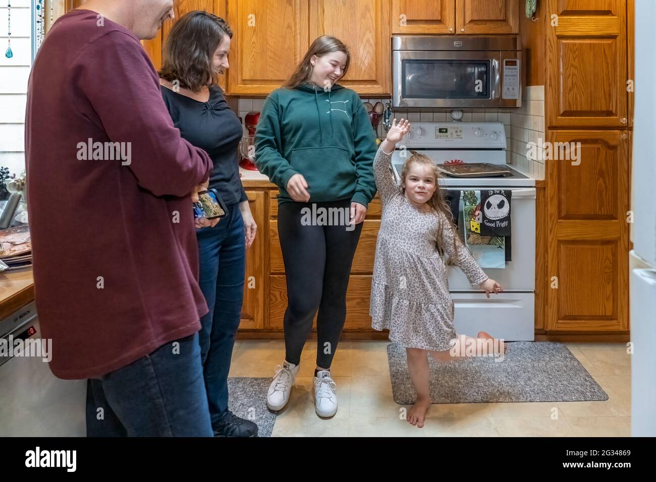 Die vierjährige Nichte, die für ihre Tante, ihren Onkel und ihren Cousin in einer Küche dumm agiert. (MR) Stockfoto