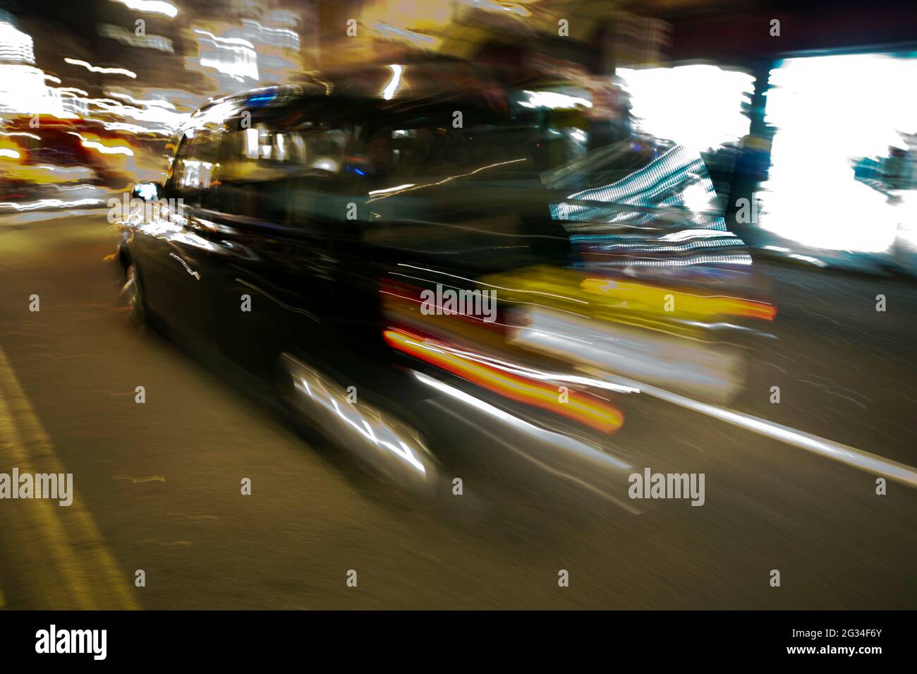 Verschwommenes Bild eines schwarzen Londoner Taxis, das nachts auf einer Straße fährt Stockfoto