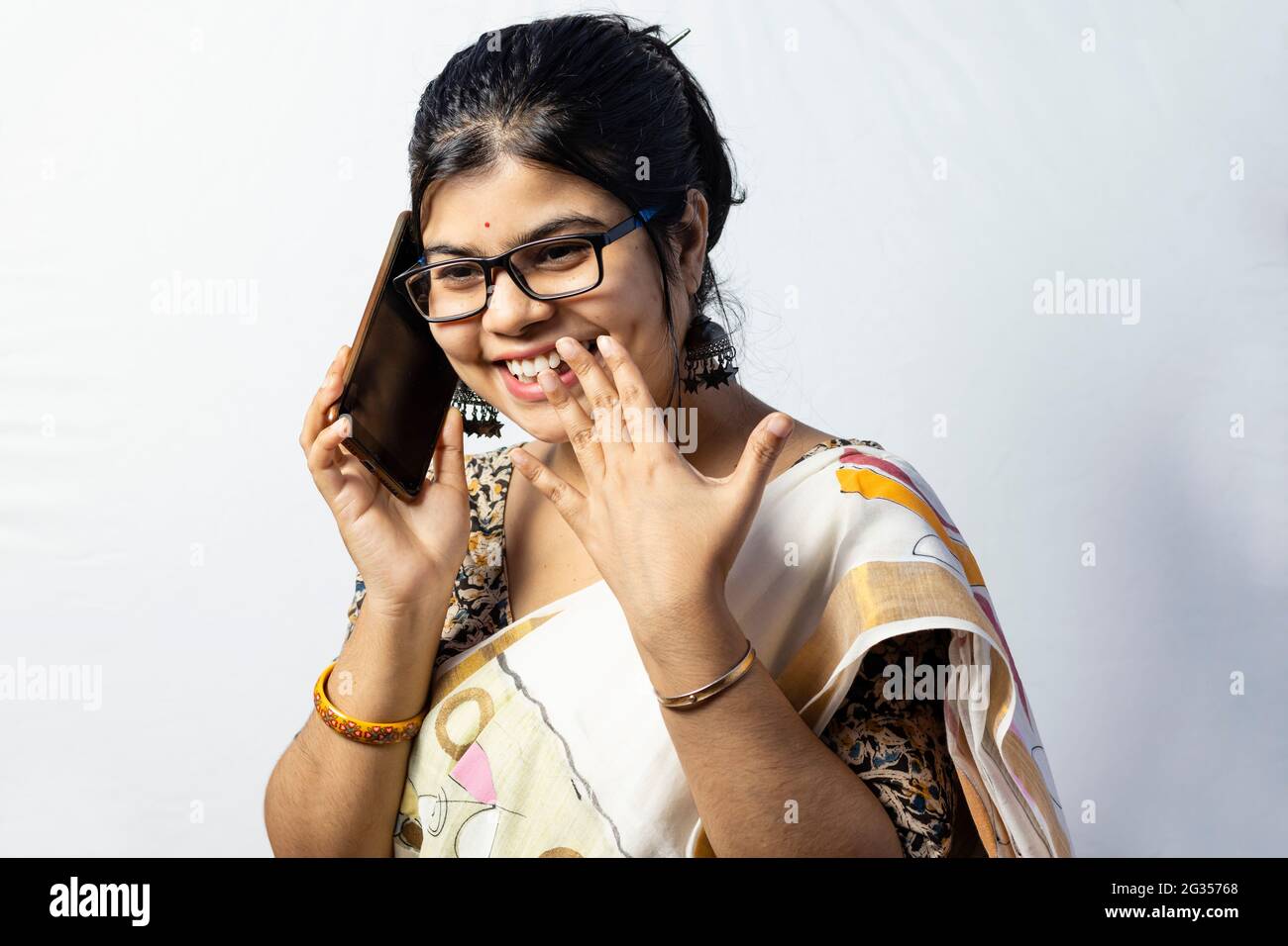 Eine wunderschöne indische Frau im Saree, die über ein Smartphone spricht und isoliert auf weißem Hintergrund lächelt Stockfoto