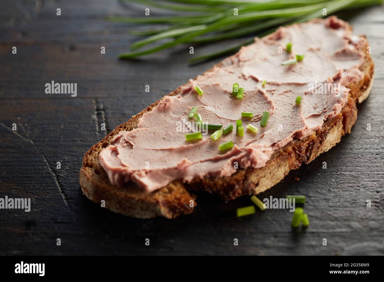 Nahaufnahme eines offenen Sandwiches mit appetiteller Leber und grünen Zwiebeln, serviert auf einem Holztisch Stockfoto
