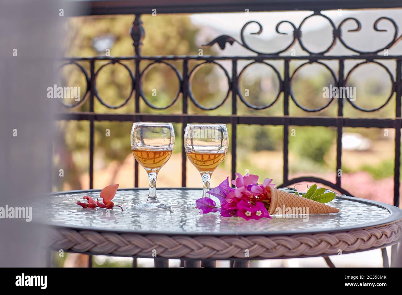 Blick vom Balkon. Glasess Weine mit rosa Blüten von Bougainvillea auf Glastisch. Erfrischungskonzept. Sommer grelle surreale Blumen und hausgemachte Getränke. Speicherplatz kopieren. Hochwertige Fotos Stockfoto