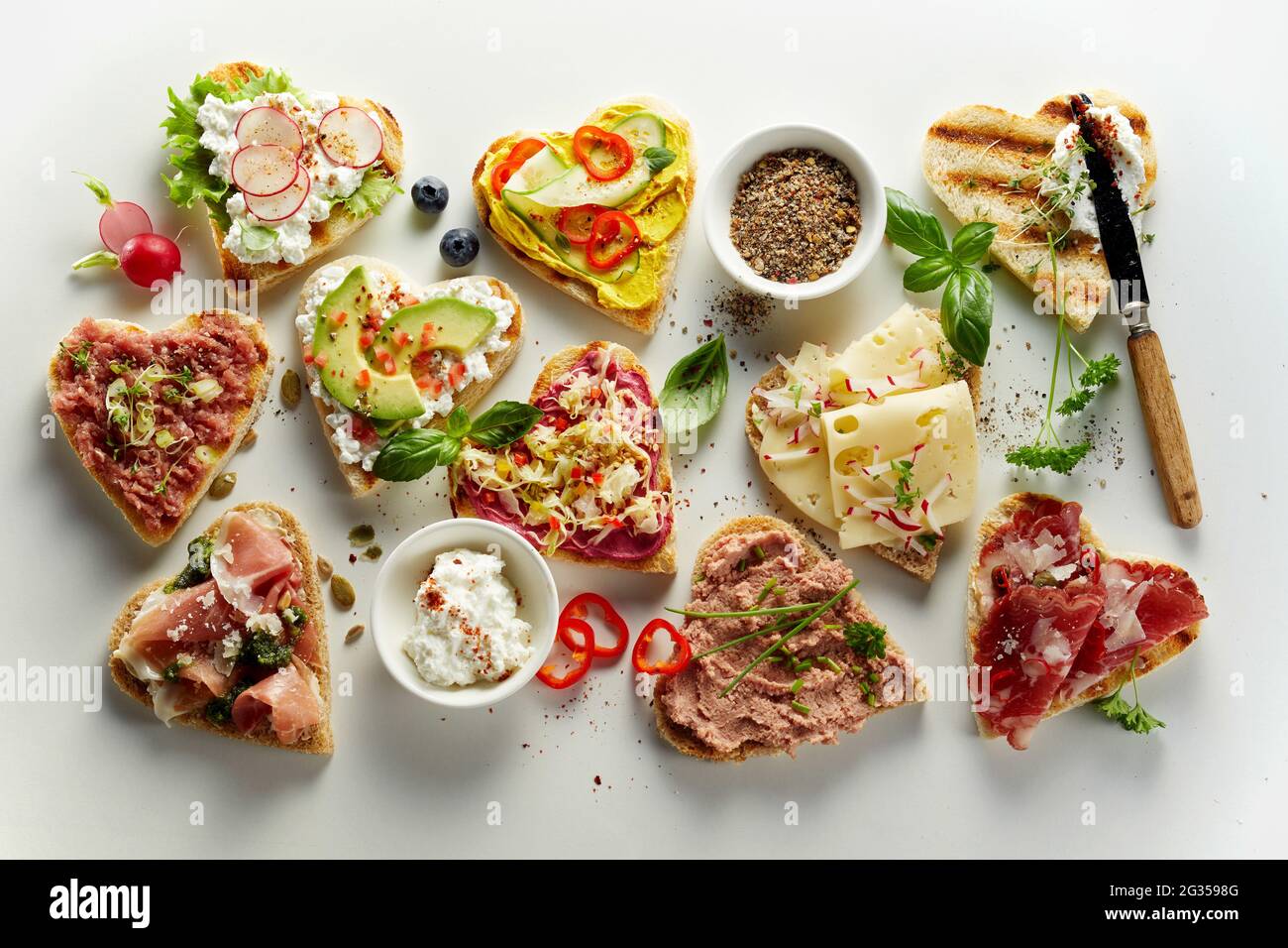Von oben auf einem weißen Tisch mit verschiedenen, appetitlich offenen Sandwiches in Herzform Stockfoto