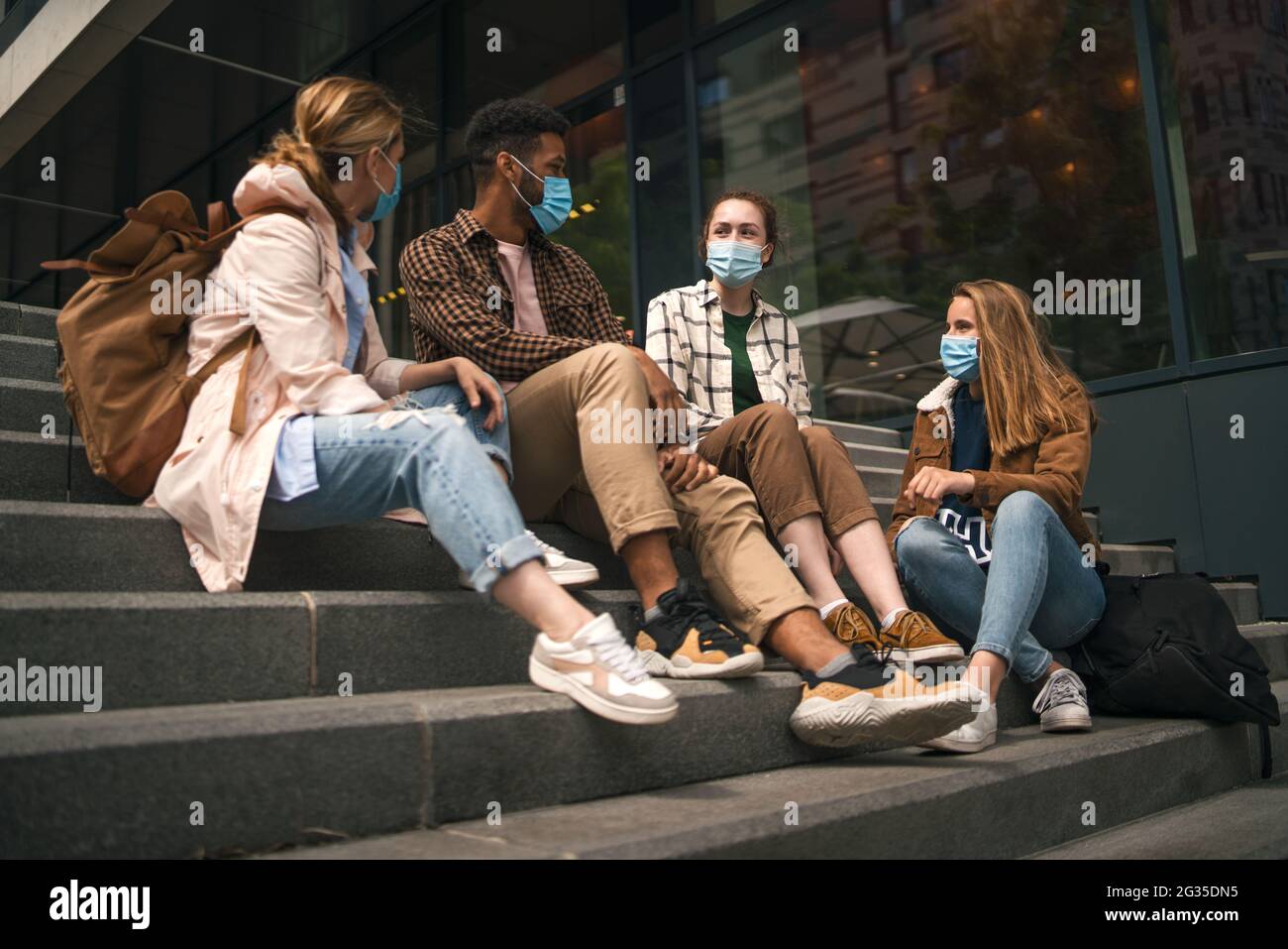 Gruppe von Studenten Freunde im Freien sitzen und reden in der Stadt, Coronavirus und zurück zum normalen Konzept. Stockfoto