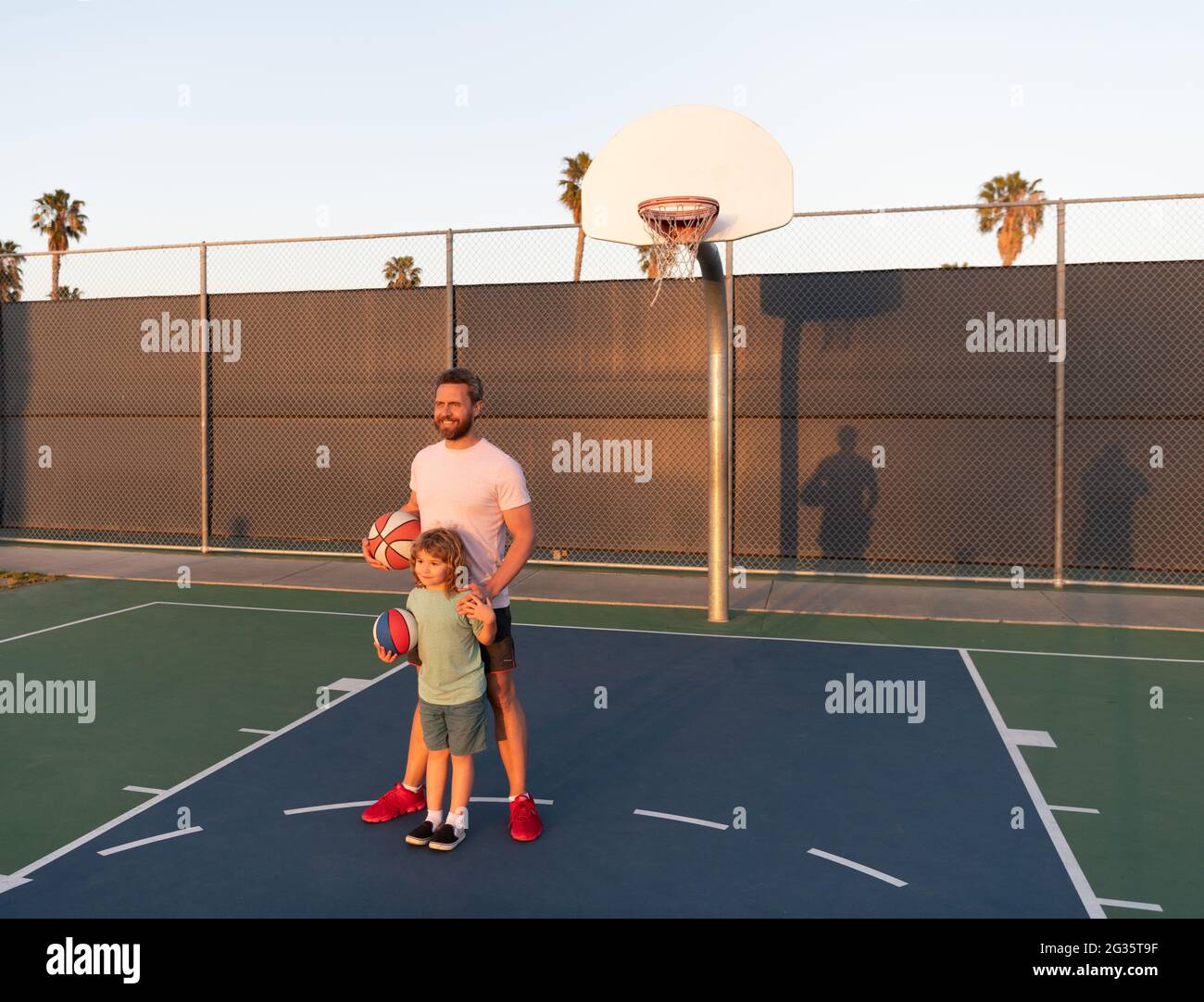 Fröhlicher Vater und Sohn spielen Basketball mit Ball auf dem Spielplatz, glückliches Wochenende Stockfoto