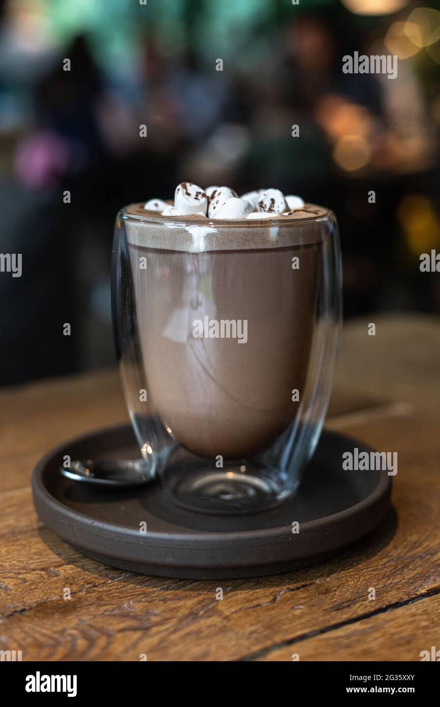 Heiße Schokolade oder Kakao-Getränk mit Salmlaw in Glas-Tasse auf Holztisch im Café. Selektiver Fokus. Getöntes Bild. Stockfoto