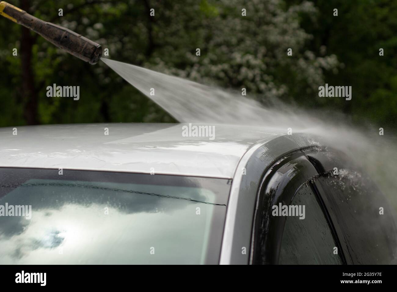 Autowäsche. Das Auto wird unter dem Druck eines Wasserstrahls gewaschen. Mit einem Wasserspray Schmutz von der Fahrzeugoberfläche abwaschen. Stockfoto