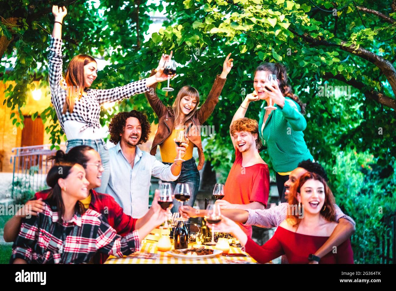 Freunde, die Spaß haben, Rotwein im Freien auf der Gartenparty zu toasten - glückliche Leute, die in der Nacht im Bauernweingut zusammen essen und trinken Stockfoto