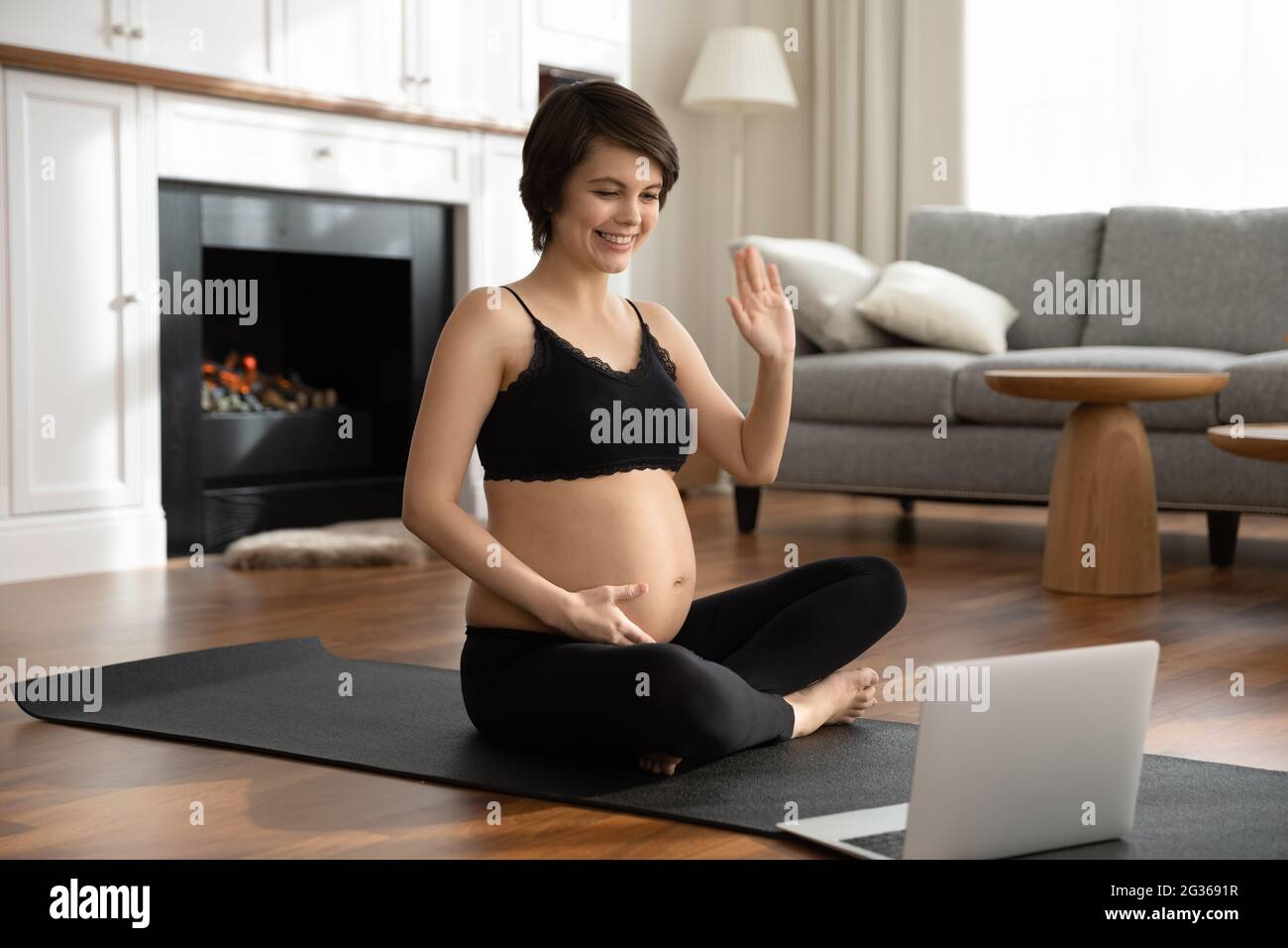 Lächelnde Schwangerin grüßt den Trainer und bereitet sich auf das Online-Training vor Stockfoto