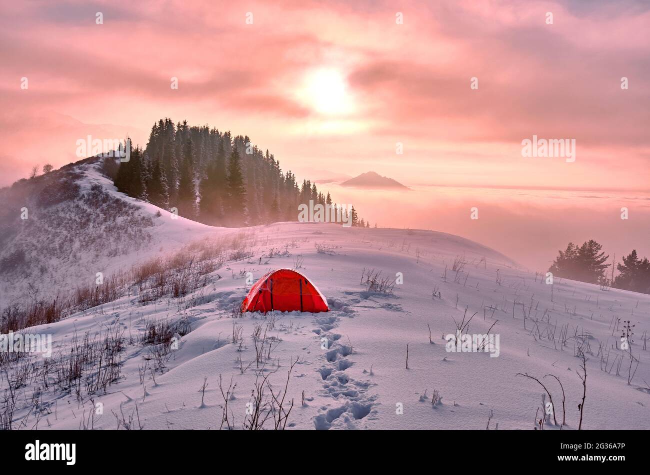 Romantischer Campingplatz in einer verschneiten Lichtung im Hochland in der Wintersaison; geheimnisvolle Wolkenstimmung in den Bergen bei Sonnenuntergang Stockfoto