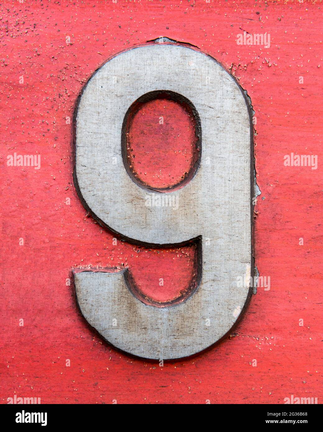 Figur 9 aus Metall auf rot lackiertem Hintergrund Stockfoto