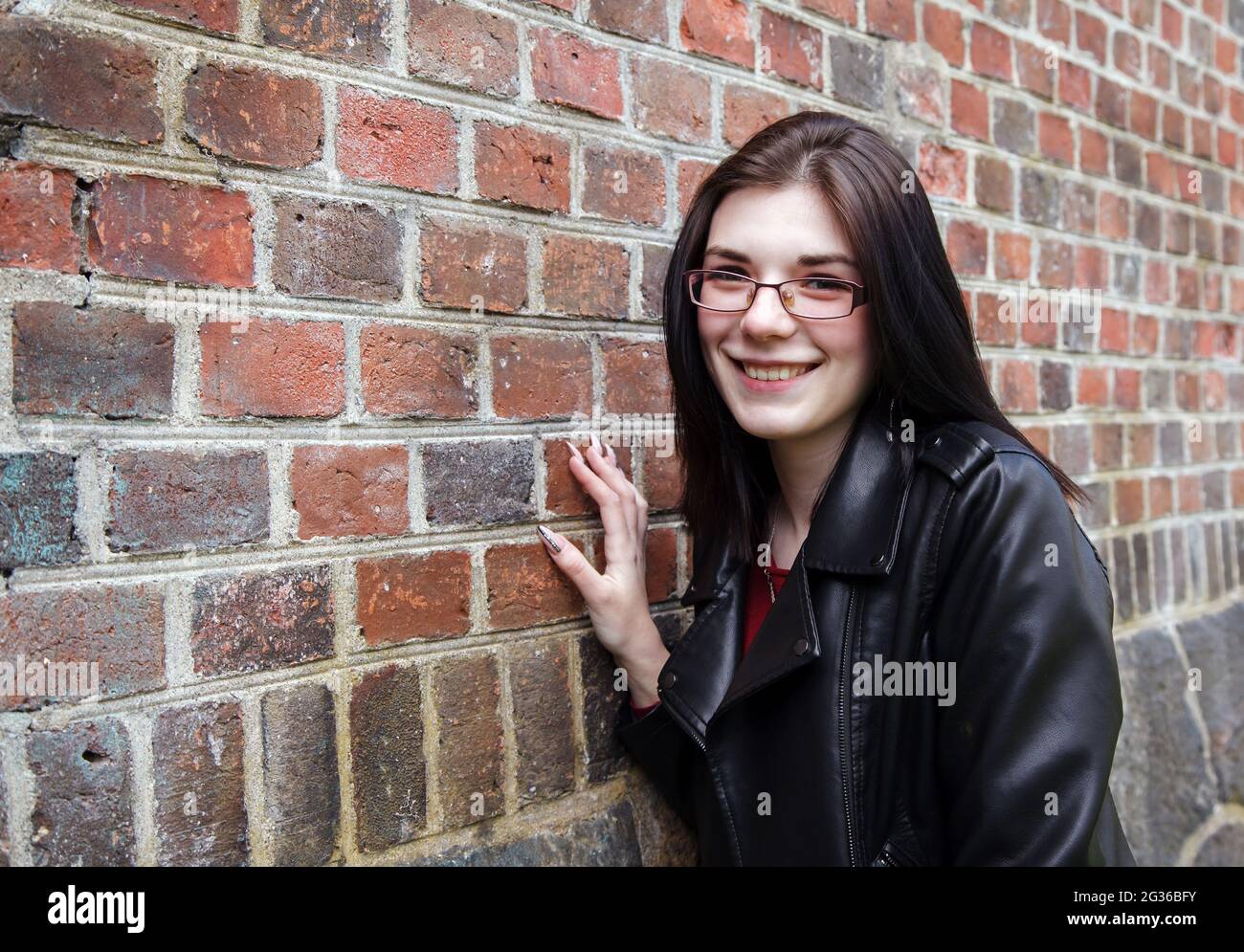 Junge schöne Mädchen in schwarzer Jacke und Jeans steht in der Nähe der alten Festungsmauer an sonnigen Tag. Nahaufnahme im Freien Stockfoto