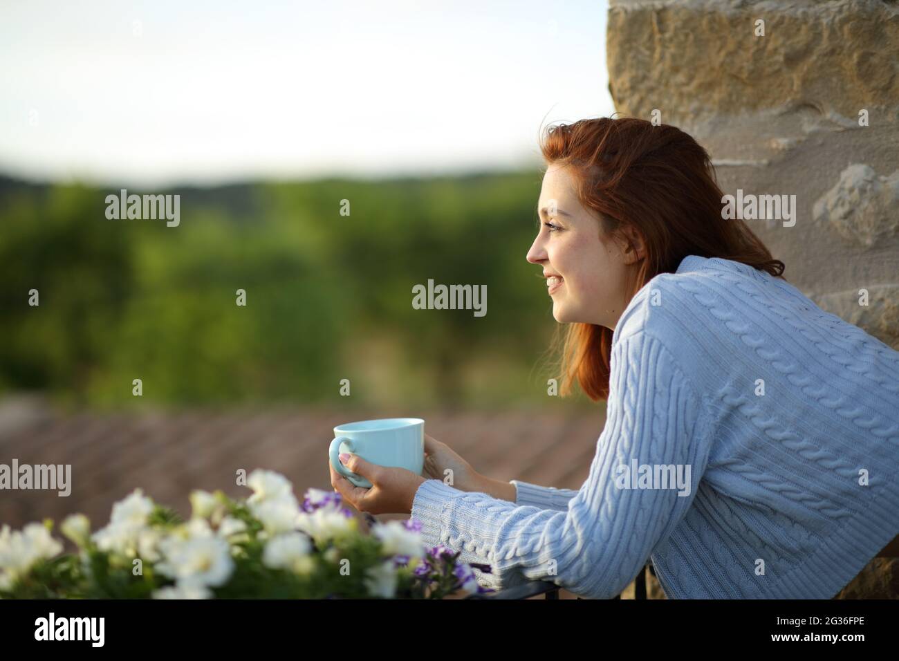Seitenansicht Porträt einer glücklichen Frau, die vom Balkon aus mit einer Kaffeetasse kontempliert Stockfoto
