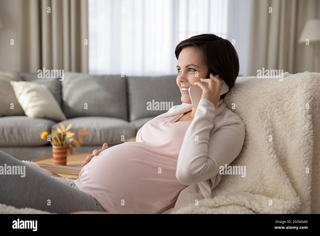 Lächelnde, schwanger Frau, die zu Hause telefoniert und den Bauch berührt Stockfoto