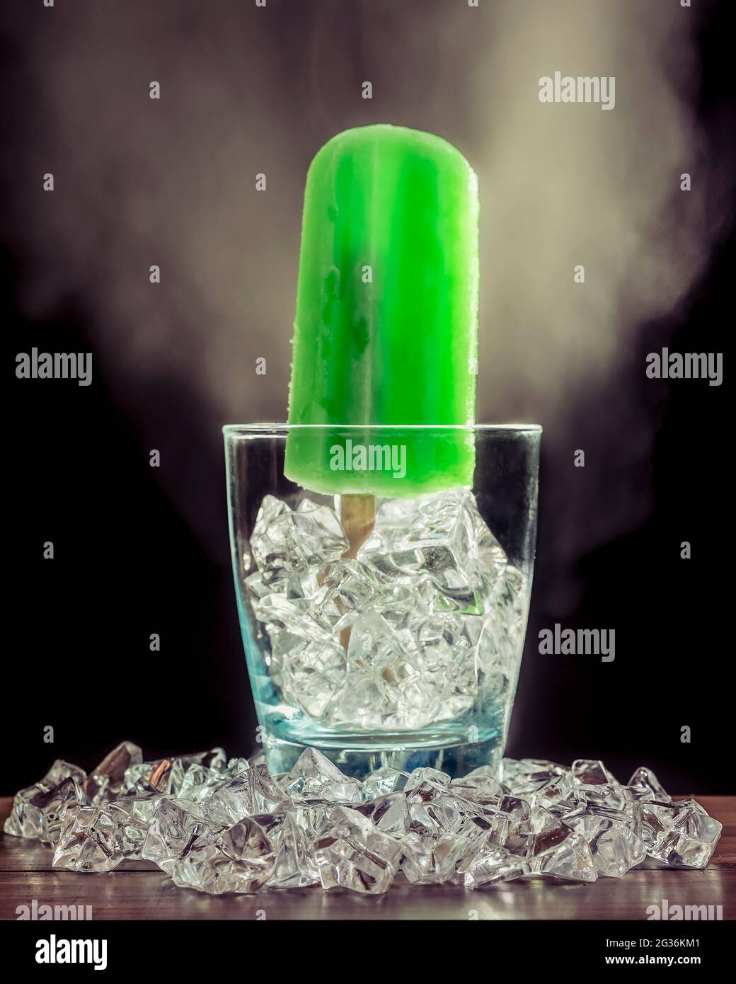 In einem Glas mit Eis und Rauch auf dunklem Grund steht ein grüner Minzpopsicle Stockfoto