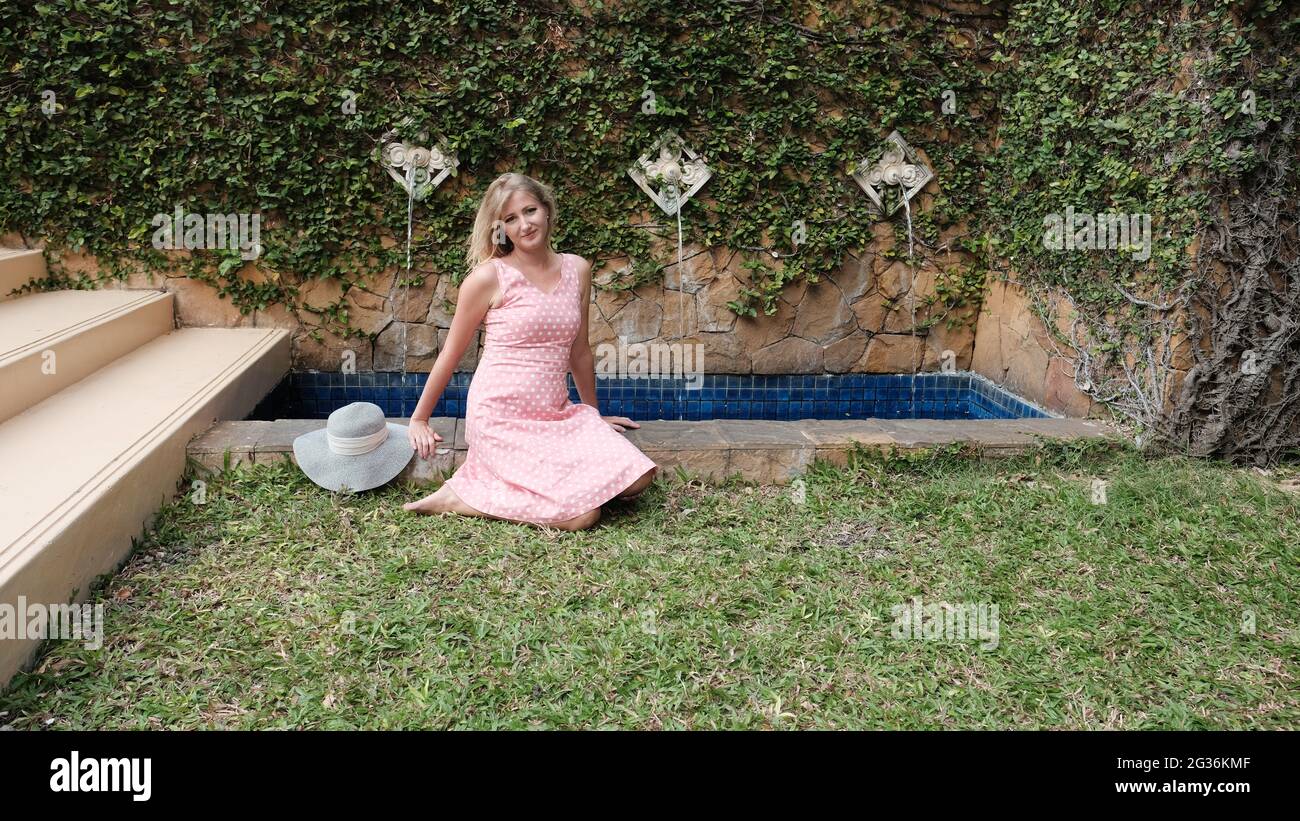 Blonde Haare kaukasischen mittleren Alters Frau Rosa Kleid draußen im Park Setting Tag weißen Hut Stockfoto