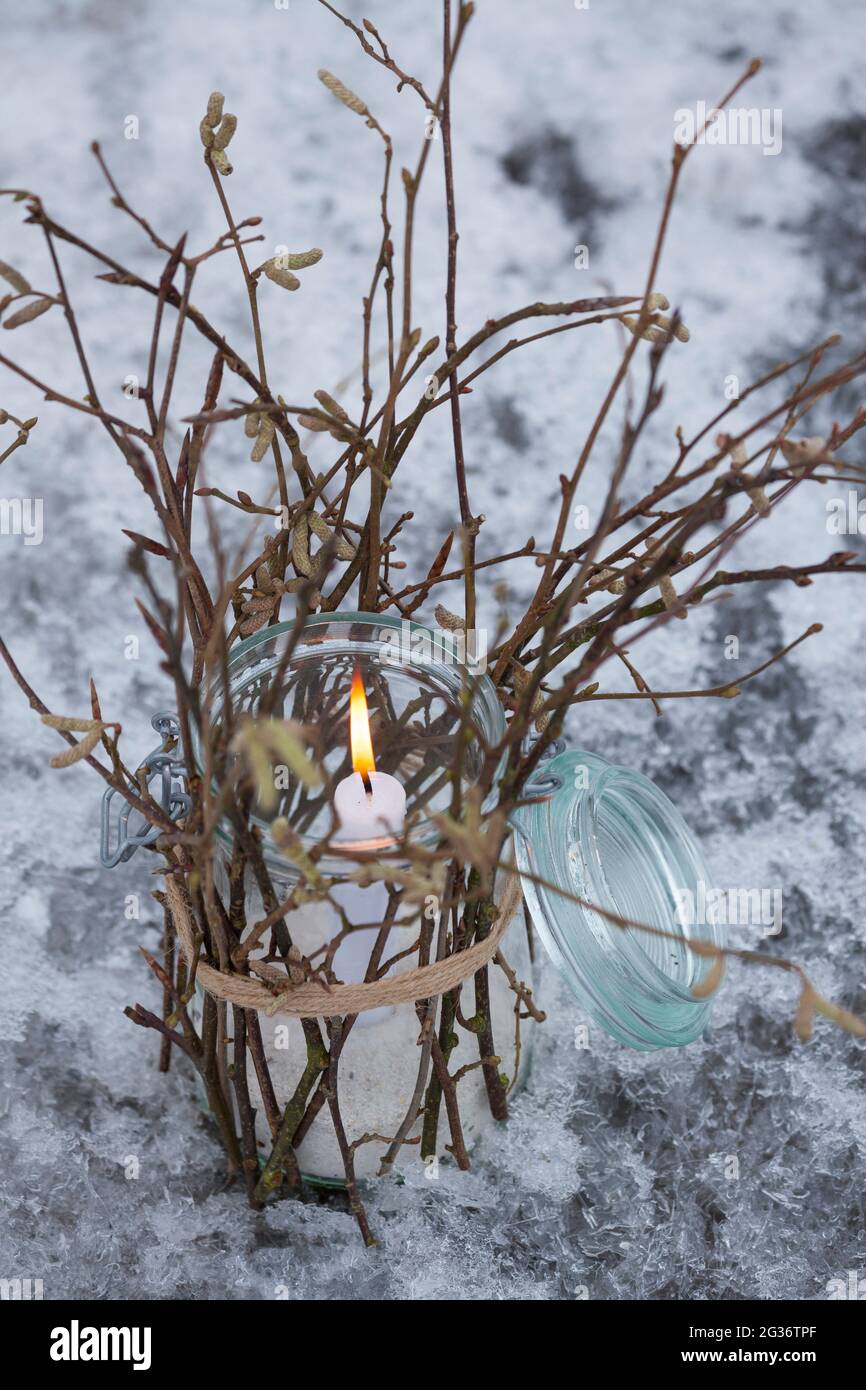 Laterne, ein Glas ist von außen mit Stöcken, Zweigen, Zweigen verziert. Eine Kerze steht und brennt im Glas, geschützt vom Wind, Stockfoto