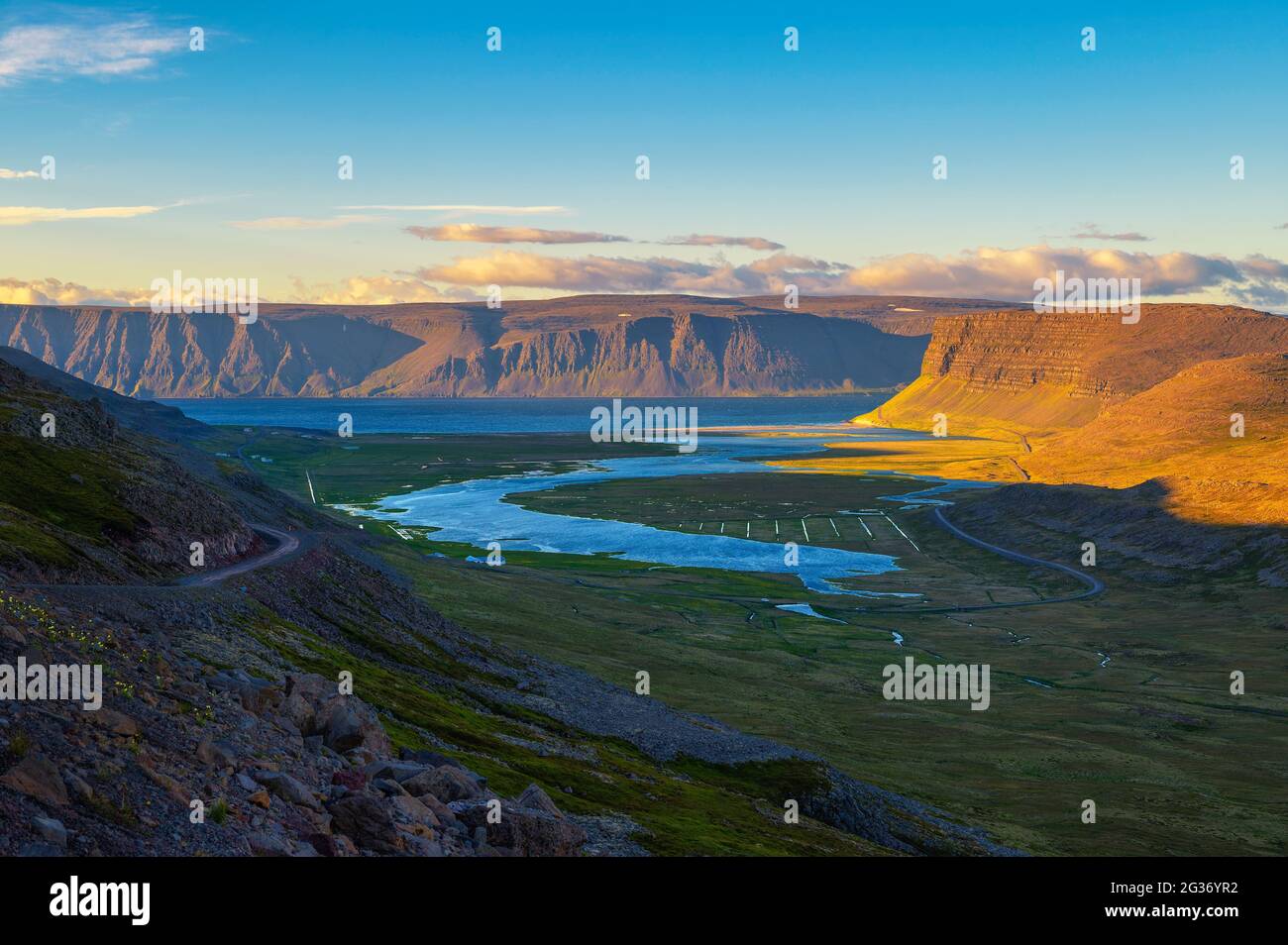 Isländische Landschaft mit Fjord und Schotterstraße bei Sonnenuntergang in Westfjorden, Island Stockfoto