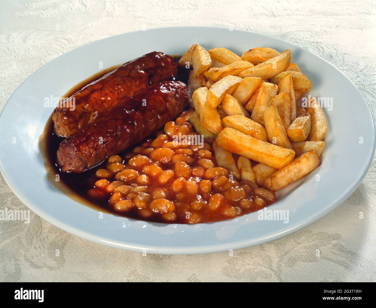 Teller mit 2 Würstchen, Chips, gebackenen Bohnen und Soße auf einem weißen Teller auf weißem strukturiertem Hintergrund Stockfoto