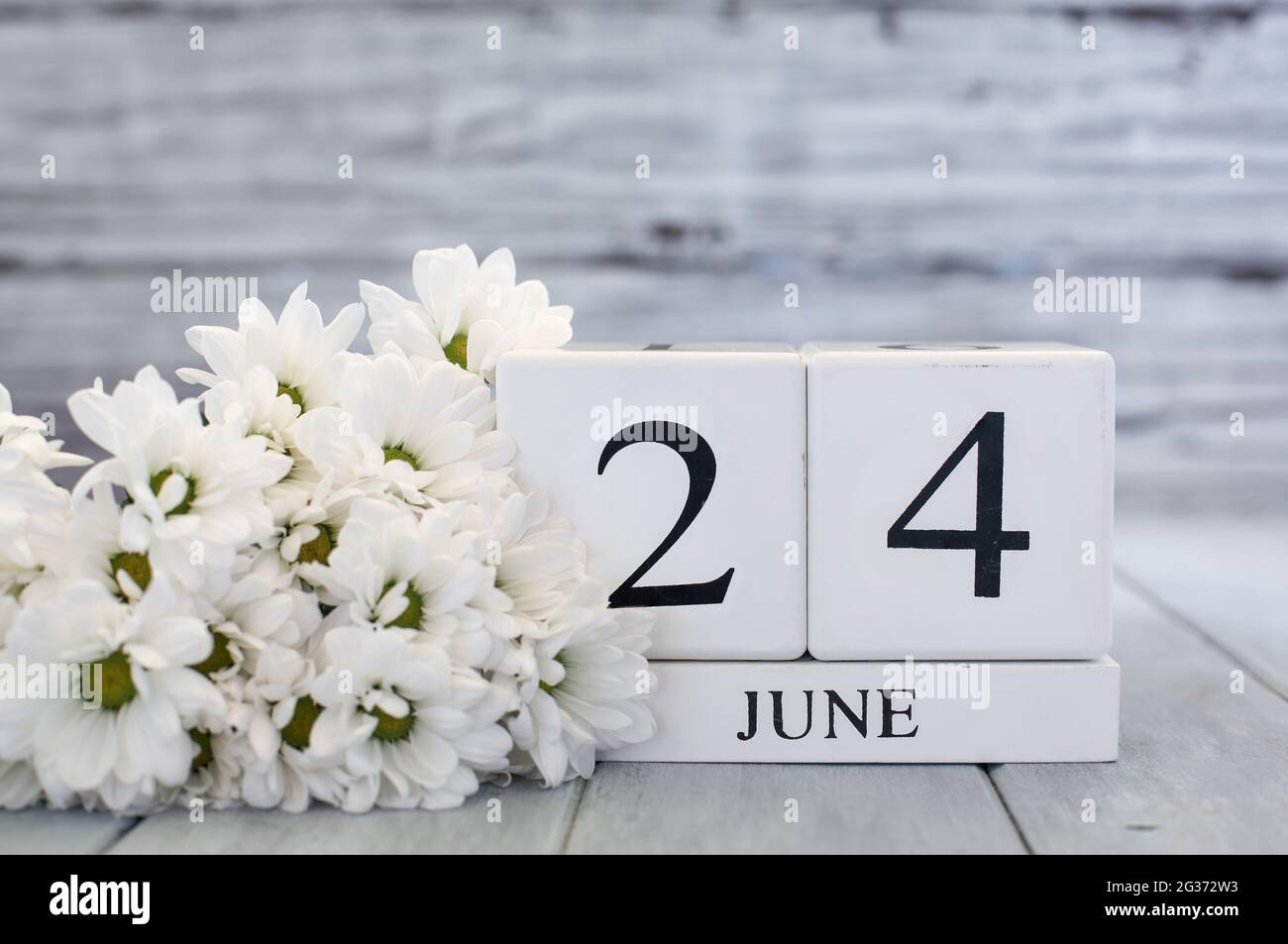 Kalenderblöcke aus weißem Holz mit dem Datum 24. Juni und weißen Gänseblümchen. Selektiver Fokus mit unscharfem Hintergrund. Stockfoto