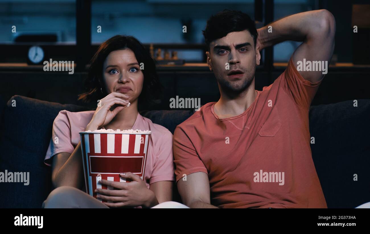 Angewiderte Frau, die Popcornkübel in der Hand hielt und sich einen Film mit einem schockierten Freund ansah Stockfoto