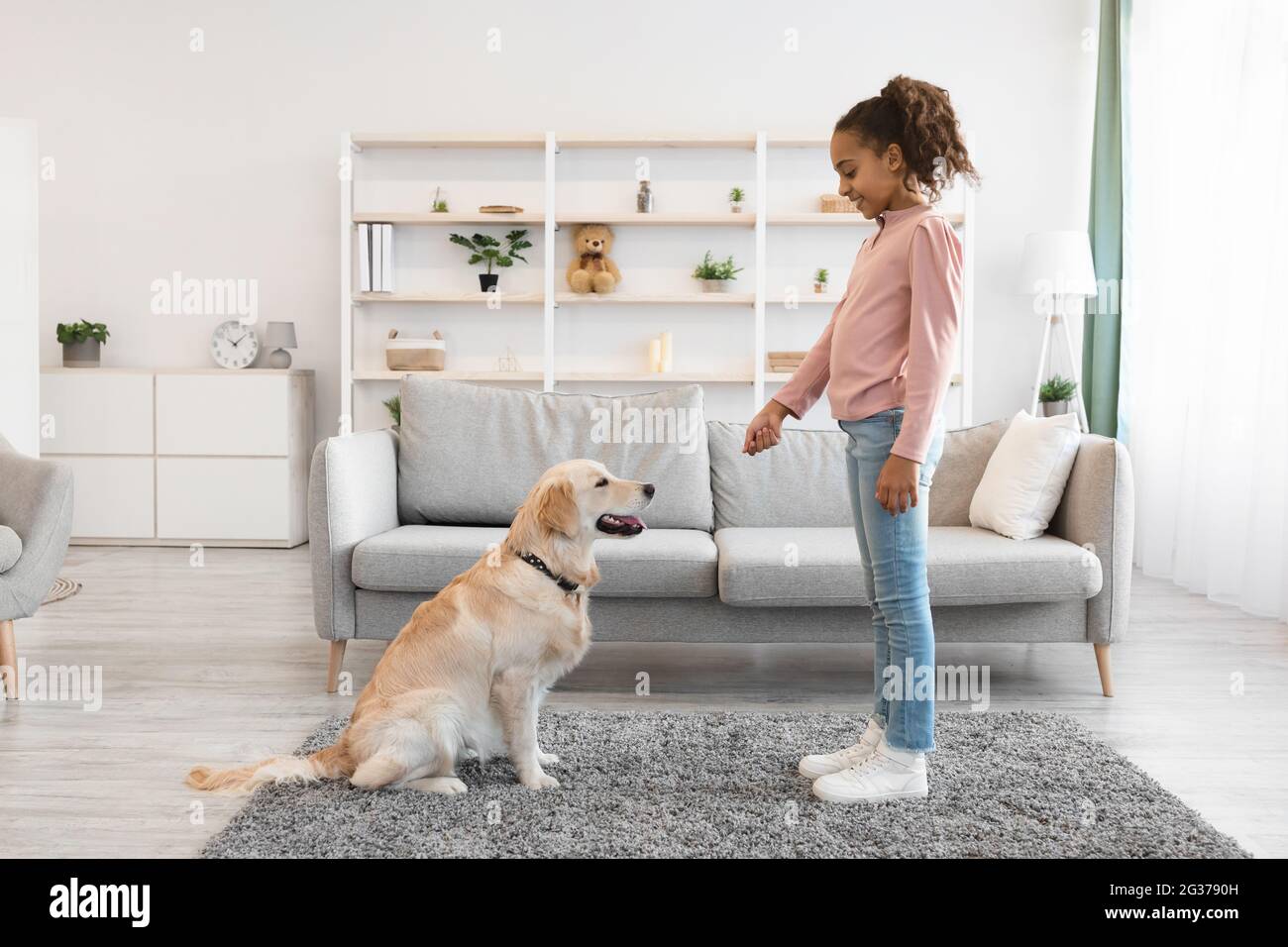 Glückliches schwarzes Mädchen, das ihrem gehorsamen Hund eine Freude macht Stockfoto