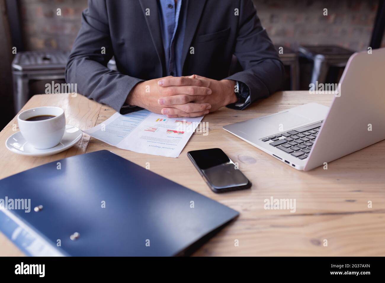 Mittlerer Teil des Geschäftsmannes sitzt, während mehrere Bürogeräte auf dem Tisch in einem Café Stockfoto