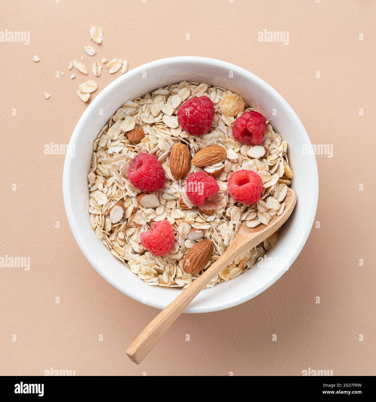 Trockenes Hafermüsli mit Mandeln und frischen Himbeeren in Schale auf beigem Hintergrund, Draufsicht. Konzept der Gewichtsabnahme, Fitness-Lifestyle, saubere Ernährung Stockfoto