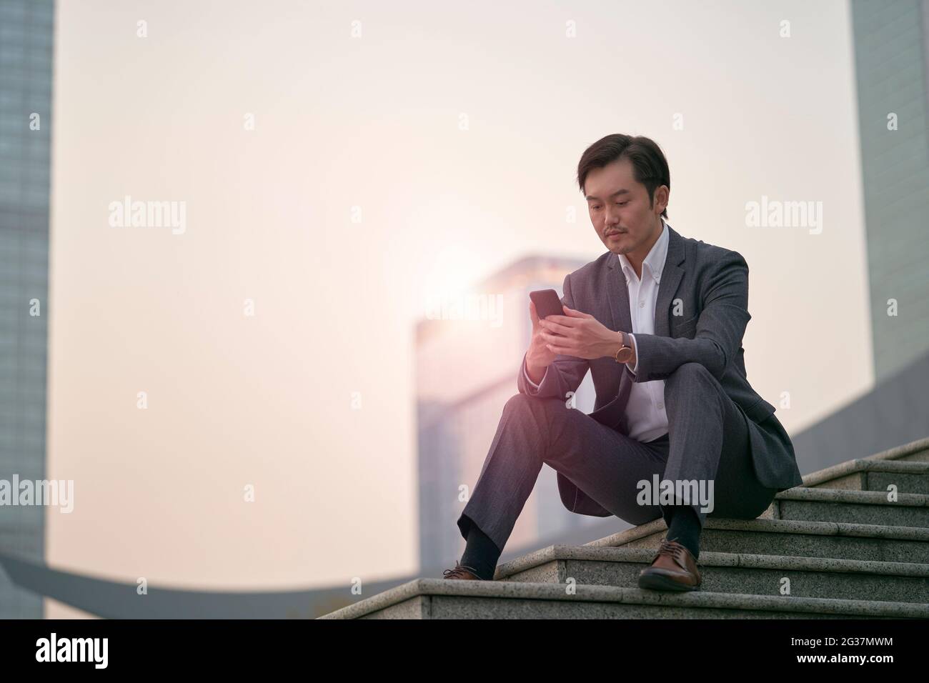 asiatische Unternehmensleitung sitzt auf einer Treppe und blickt auf das Mobiltelefon Stockfoto