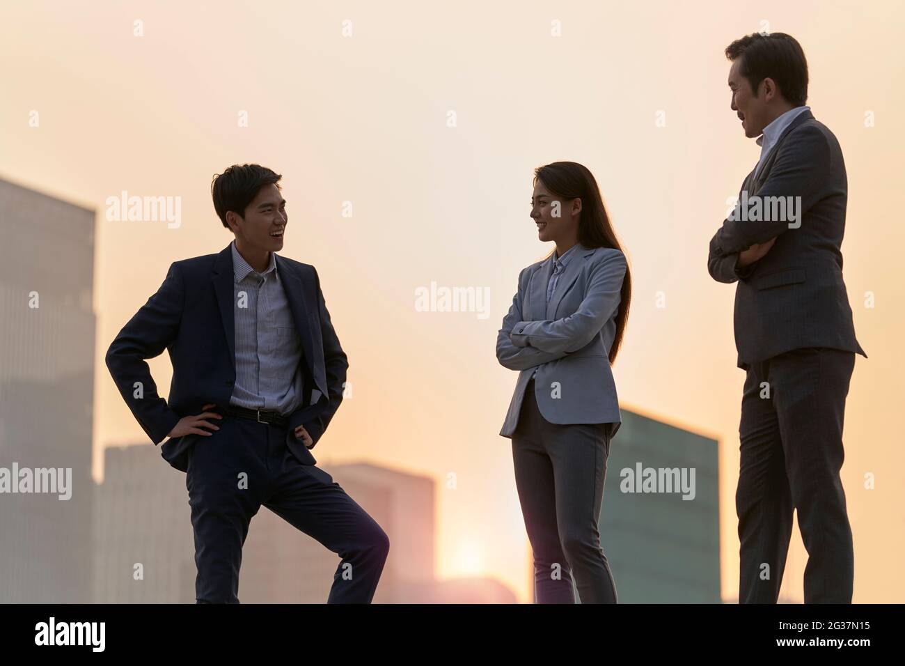 Team von asiatischen Unternehmensleitern, die auf einer Plattform stehen und sich mit Gesprächen unterhalten, die in der Abenddämmerung mit Stadthintergrund unterhalten Stockfoto