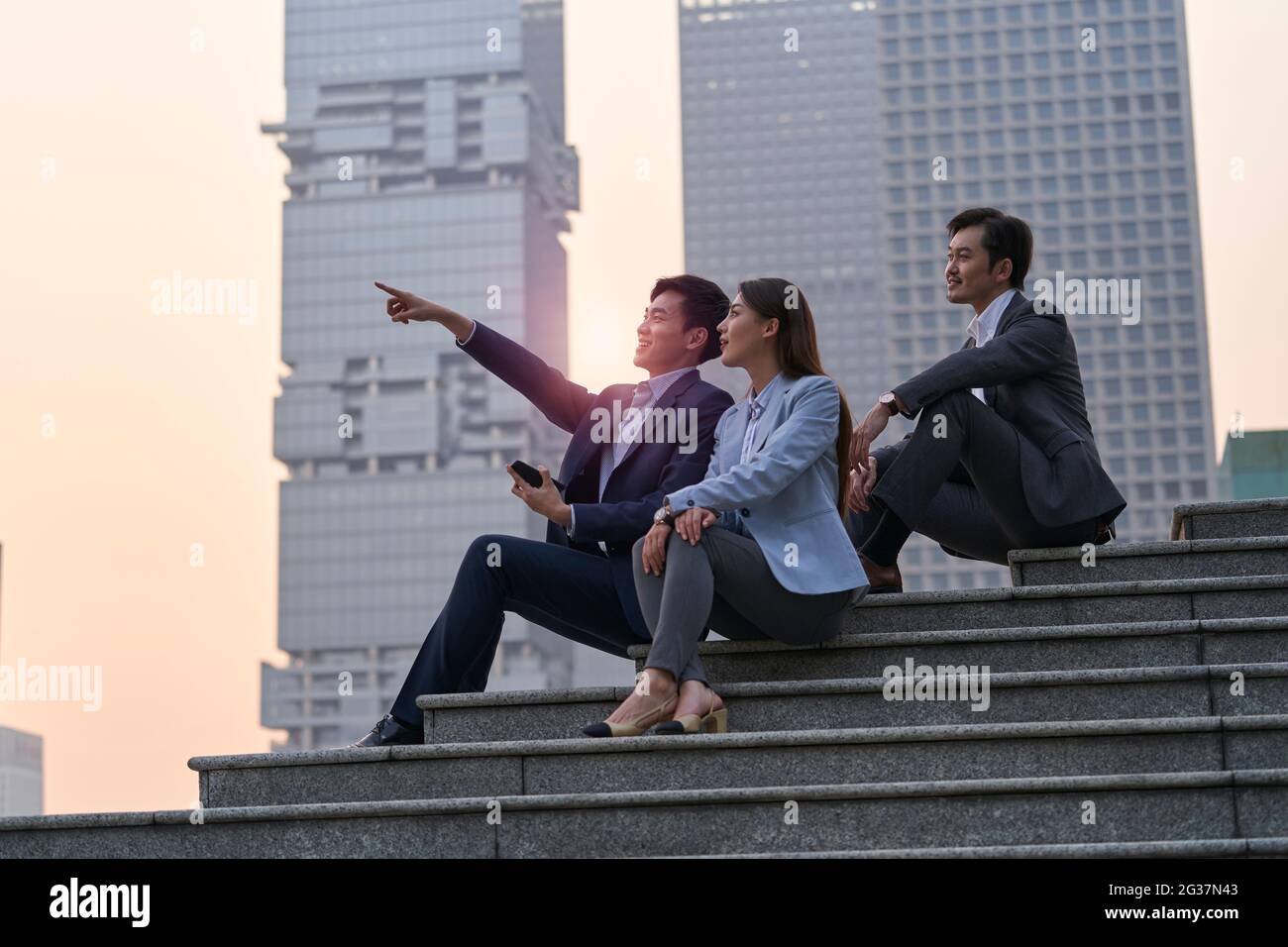 Drei asiatische Führungskräfte sitzen auf einer Treppe und unterhalten sich entspannt Stockfoto