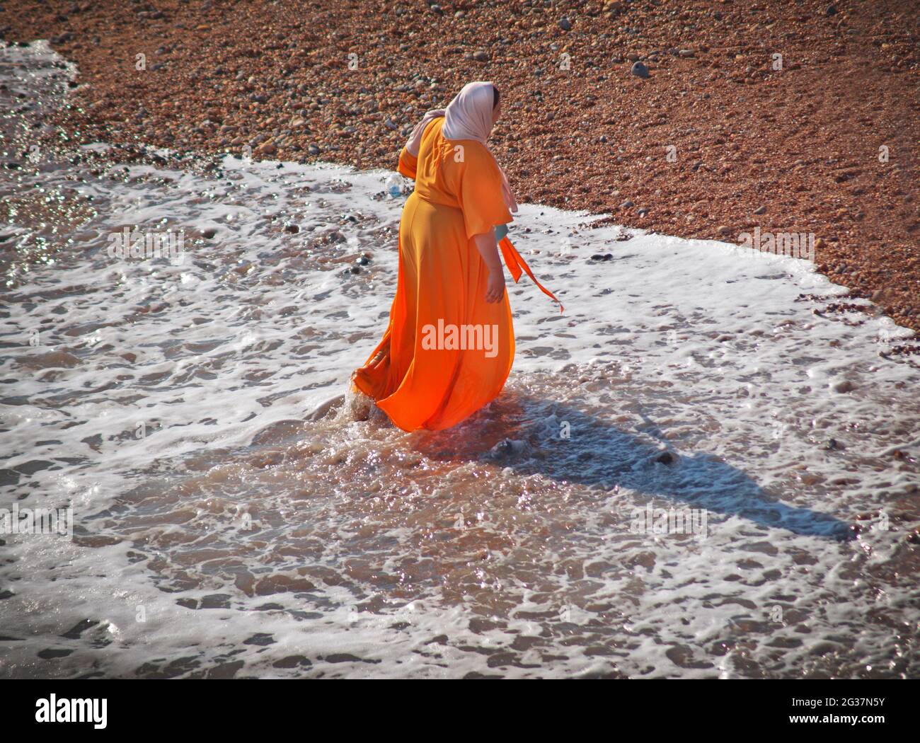 Eine Frau in einem orangefarbenen Kleid paddelt im Meer von Brighton Stockfoto