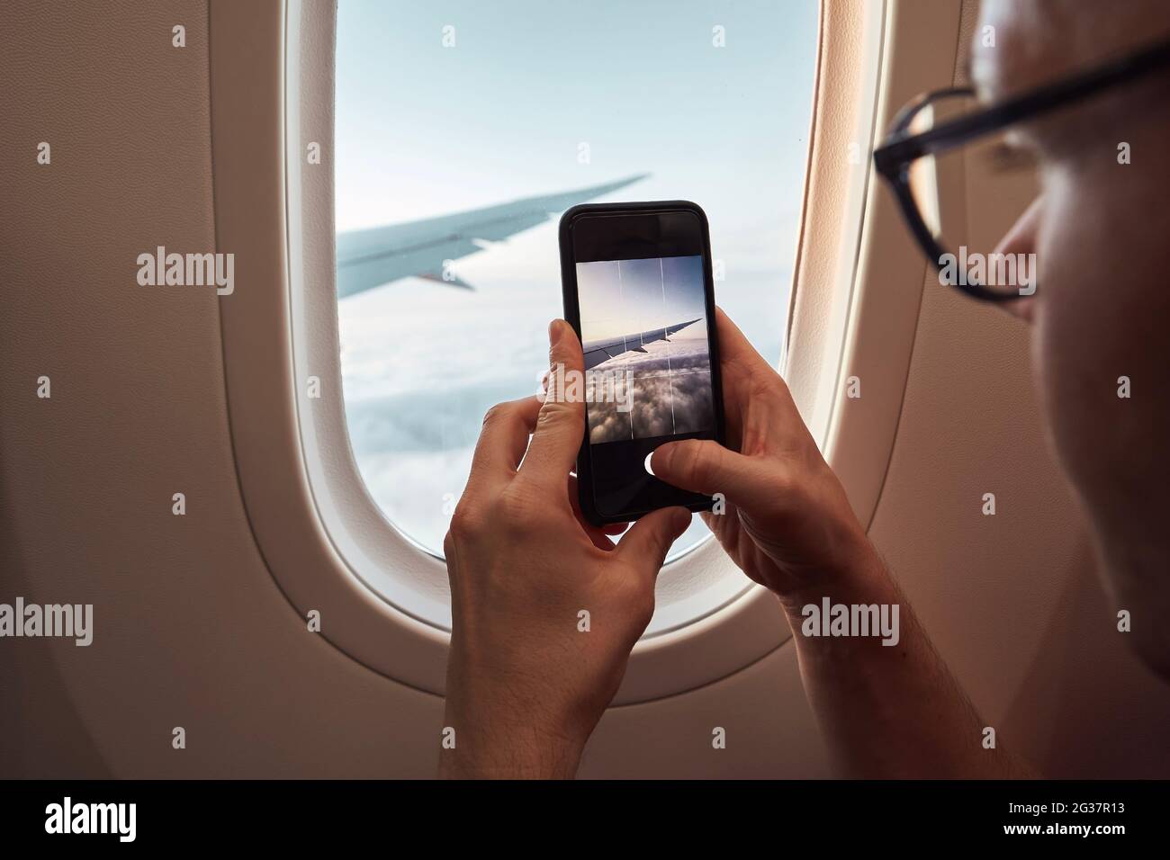 Passagier fotografiert durch das Flugzeugfenster. Mann, der Smartphone während des Fluges über Klumpen benutzt. Themen Reisen, Verbindung und Erinnerungen. Stockfoto