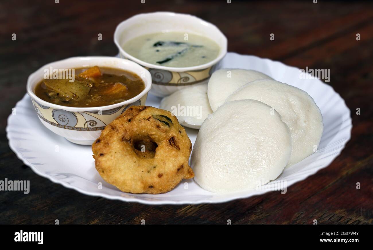 Südindisches Frühstücksmenü, Idid Vadai mit Kokosnuss-Chutney und Sambar, serviert auf einem weißen Keramikteller auf einem Holztisch. Stockfoto