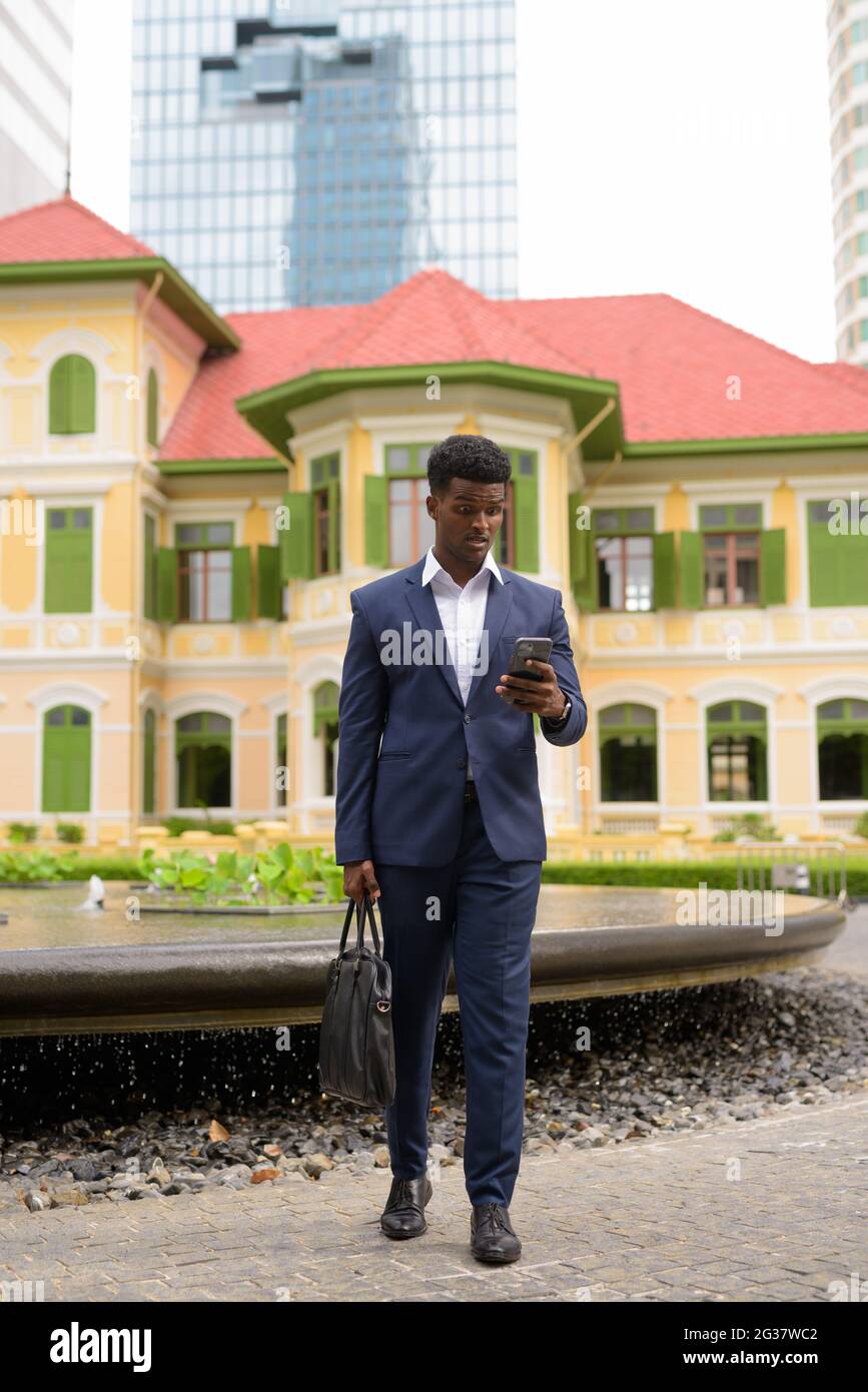 In voller Länge Aufnahme von schockierten und überrascht afrikanischen Geschäftsmann im Freien tragen Anzug und SMS mit Handy vertikale Aufnahme Stockfoto