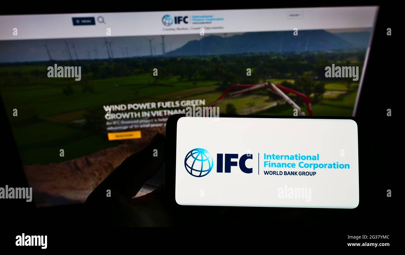 Person, die das Smartphone mit dem Logo der Institution International Finance Corporation (IFC) auf dem Bildschirm vor der Website hält. Konzentrieren Sie sich auf die Telefonanzeige. Stockfoto
