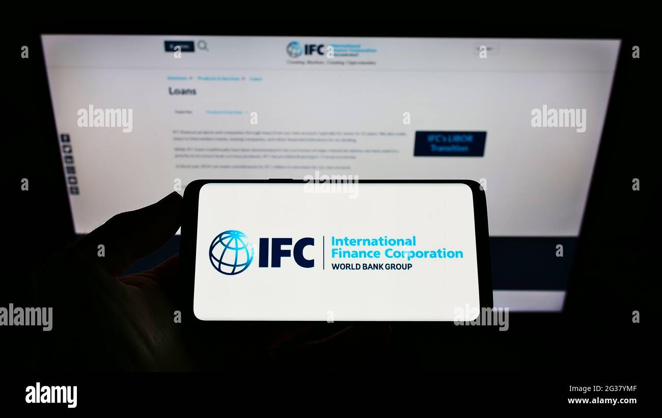 Person mit Mobiltelefon und Logo der Institution International Finance Corporation (IFC) auf dem Bildschirm vor der Webseite. Konzentrieren Sie sich auf die Telefonanzeige. Stockfoto