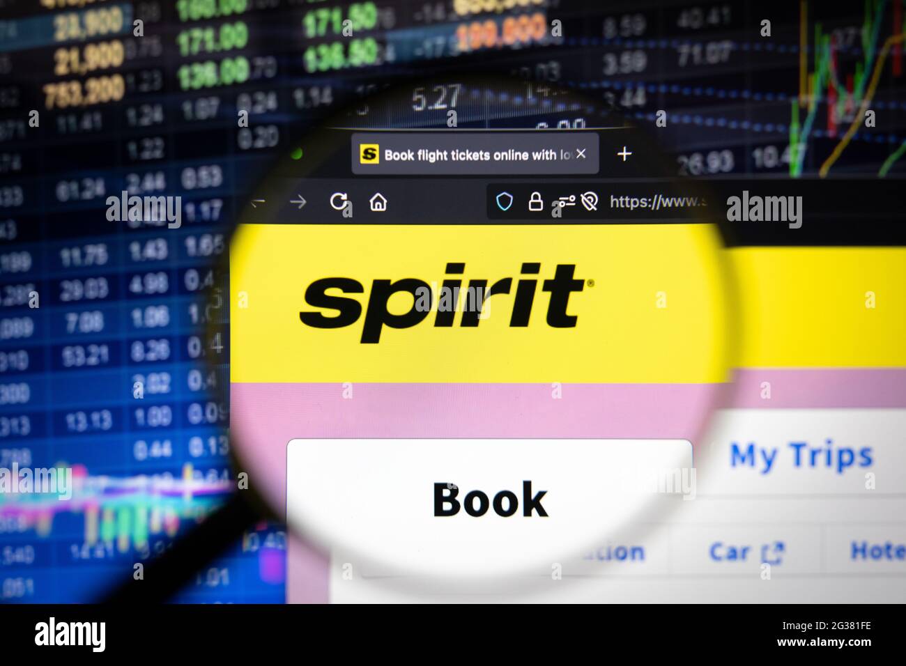 Spirit Airline Firmenlogo auf einer Website mit verschwommenen Börsenentwicklungen im Hintergrund, die auf einem Computerbildschirm durch eine Lupe gesehen werden Stockfoto