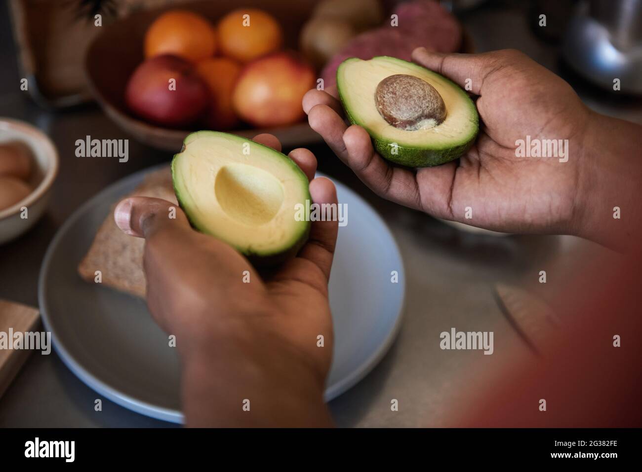Afrikanischer Mann, der zwei Hälften einer Avocado in seiner Küche hält Stockfoto