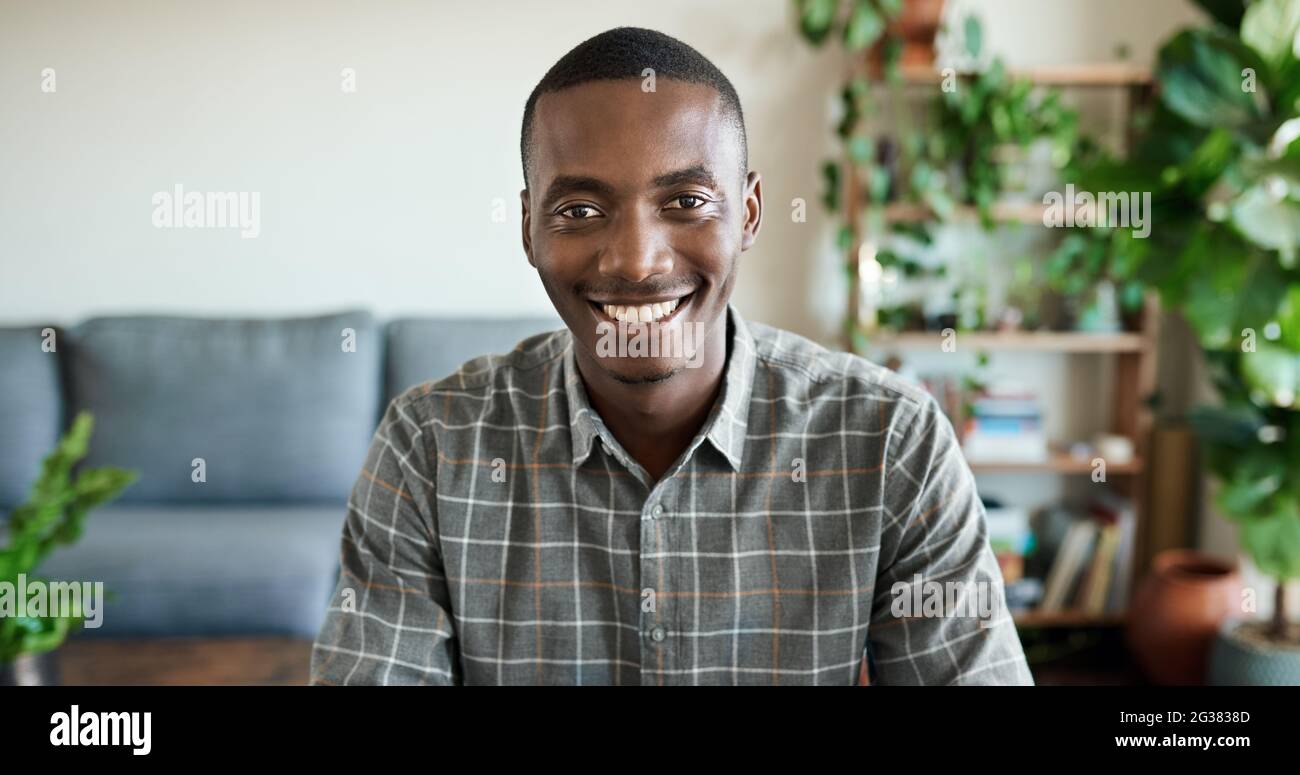 Lächelnder junger afrikanischer Mann, der von zu Hause aus in seinem Wohnzimmer arbeitet Stockfoto