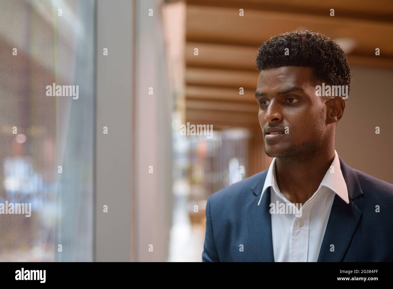 Porträt eines afrikanischen Geschäftsmannes, der durch das Fenster in horizontaler Aufnahme schaute Stockfoto