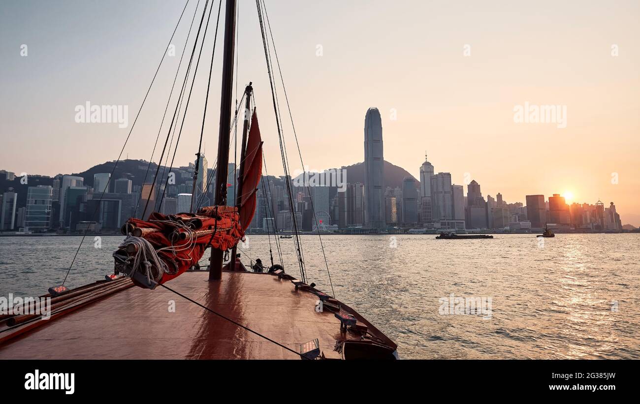 Traditionelles Junk-Boot über den Victoria Harbour und die Skyline von Hongkong mit Wolkenkratzern bei schönem Sonnenuntergang. Stockfoto