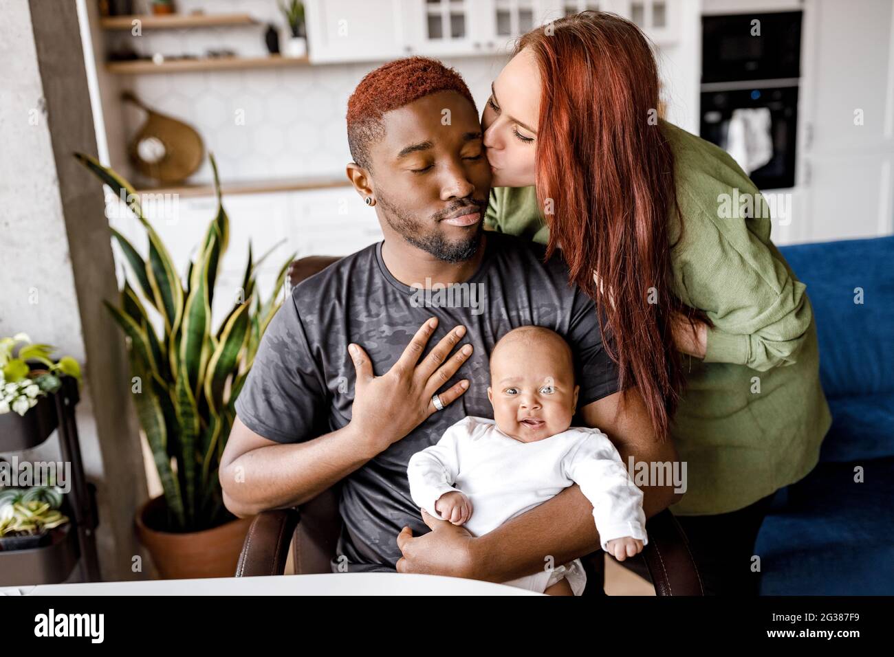 Happy afroamerikaner junger Vater sitzen mit kleinen Jungen Sohn Kind, verbringen Zeit mit jungen kaukasischen Frau, küssen Ehemann, gemischte Rasse Familie Stockfoto