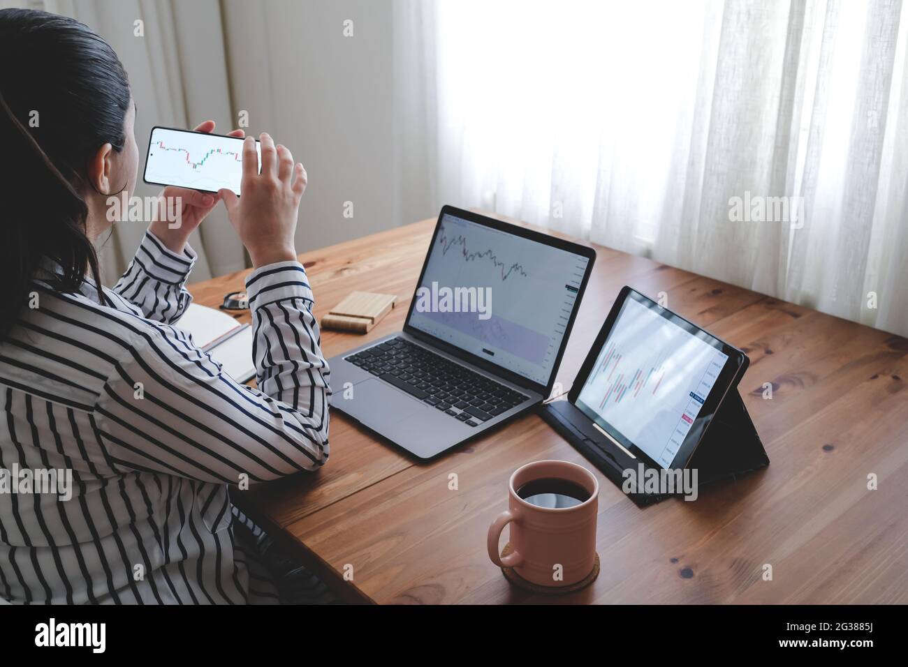 Junge Frau, die sich mit ihrem Smartphone die Börsencharts im Detail anprüft. Frau, die von zu Hause aus alle Börsencharts abarbeitet. Stockfoto