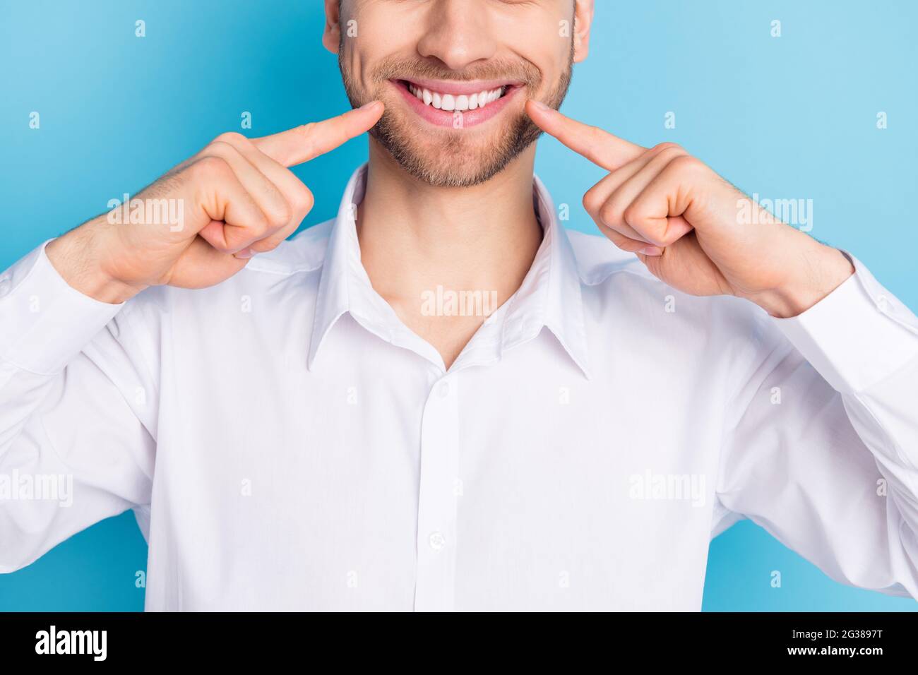 Zugeschnittenes Foto von charmanten jungen Mann zeigen Finger Zähne keramische Implantate Klinik isoliert auf blauem Hintergrund Stockfoto