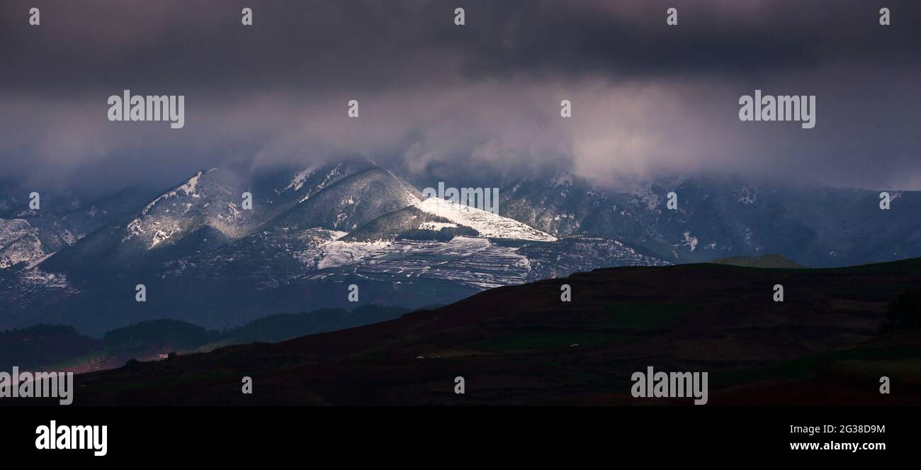 Winterbergpanorama mit dramatischen Sturmwolken, Licht im Dunkeln scheint auf dem Schneeberg. Yunnan, Südchina. Stockfoto